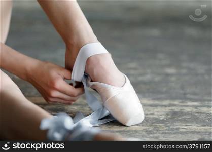 Close-up shot of a ballerina taking off the ballet shoes sitting on the floor in the studio