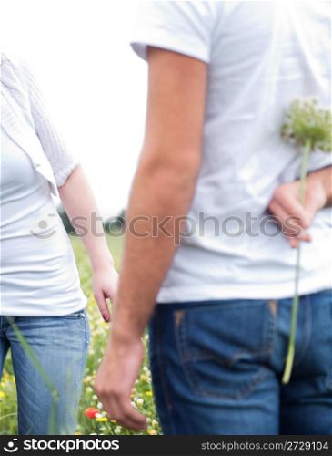 Close up shot of a boyfriend hiding a flowerr in the park