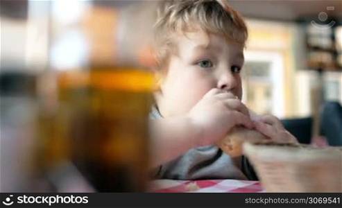 Close-up shot of a cute little boy eating a bun in a cafe