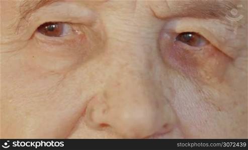 Close-up shot of a face of a senior woman with tired brown eyes and wrinkled skin