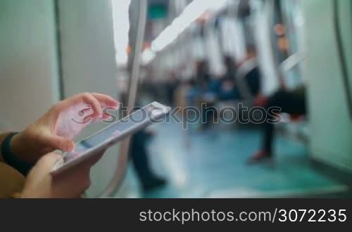 Close-up shot of a female hands using touch pad in subway train. Other passengers in blurry background