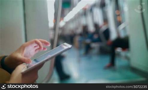 Close-up shot of a female hands using touch pad in subway train. Other passengers in blurry background