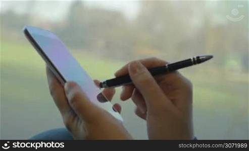 Close-up shot of a girl texting with pen on smart phone in train. Nature scenes passing in background