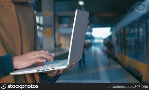 Close-up shot of a girl using laptop at the railway station. People getting on a train in background