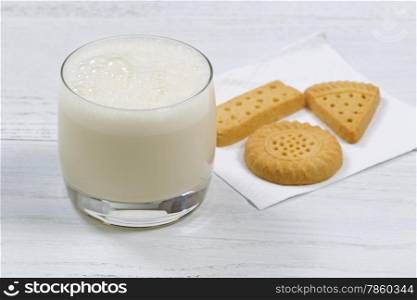 Close up shot of a glass of freshly poured milk with cookies in the background on white wooden table. Focus on front lip of glass.