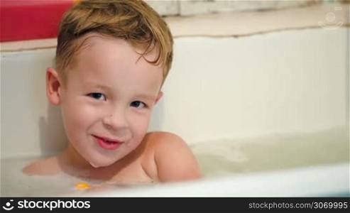 Close-up shot of a laughing little boy in the bath with toys