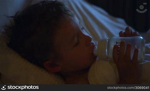Close-up shot of a little boy drinking milk from the bottle before bedtime