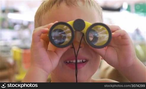 Close-up shot of a little boy looking through small binocular, then he taking it away and looking to the camera smiling