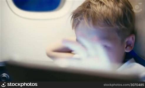 Close-up shot of a little boy playing on touch pad during in the plane. Child looking tired or bored