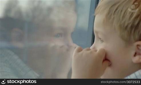 Close-up shot of a little child in the train. Boy looking out the window with hands close to face and reflection in the glass