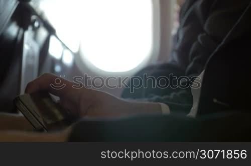 Close-up shot of a male passenger in the plane using smart phone to see a film. Entertainment during the flight