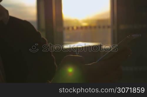 Close-up shot of a man in suit using smart phone in terminal of airport against background of evening sun shining through the window