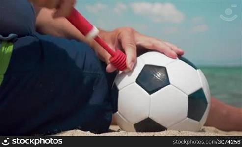 Close-up shot of a man pumping football with hand pump on the beach. Preparing for a game at the seaside
