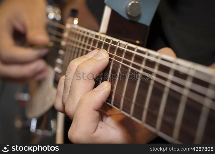 close up shot of a man with his fingers on the frets of a guitar playing