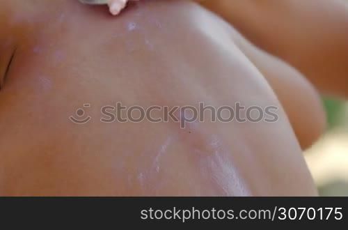 Close-up shot of a mother applying sunscreen cream on sons back