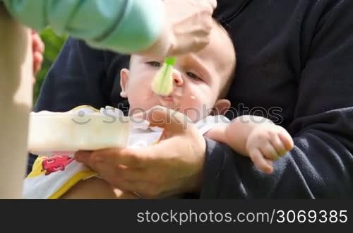 Close-up shot of a mother feeding a baby with a cereal while father holding him. Breakfast outdoor