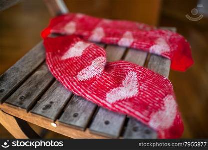 Close-up shot of a pair of red woollen socks with heart pattern lying on wooden chair. Red woollen socks on wooden chair