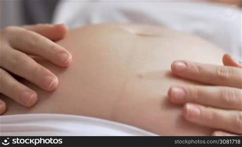 Close-up shot of a pregnant woman stroking bare belly gently and careful, baby moving inside. Healthy pregnancy