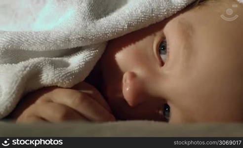 Close-up shot of a quiet little boy covered with the white towel