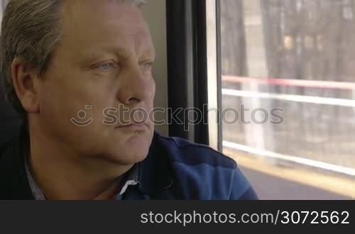 Close-up shot of a senior man having peaceful time during his travel ride. He staring through the window with thoughtful look
