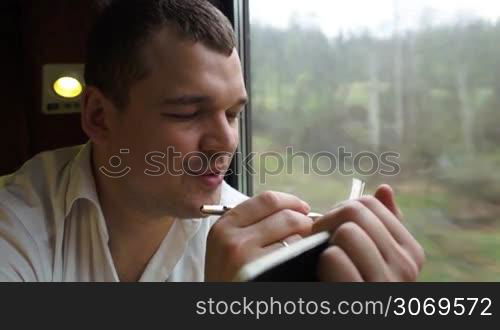 Close-up shot of a thoughtful man taking notes sitting near the window in moving train