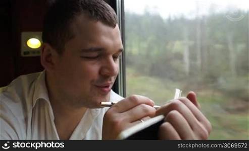 Close-up shot of a thoughtful man taking notes sitting near the window in moving train