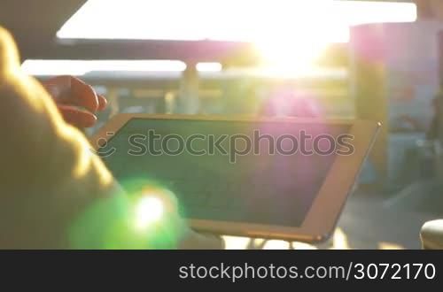 Close-up shot of a woman at the station chatting on tablet computer in the bright evening sunshine