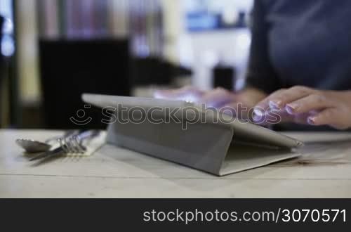 Close-up shot of a woman in cafe typing on touch pad and sending message or e-mail