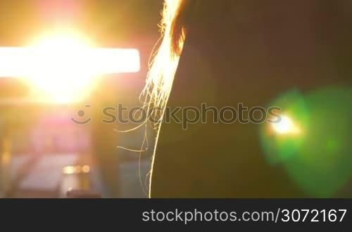 Close-up shot of a woman in the hood talking on the phone on background of bright evevning sun flare