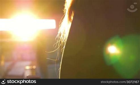 Close-up shot of a woman in the hood talking on the phone on background of bright evevning sun flare