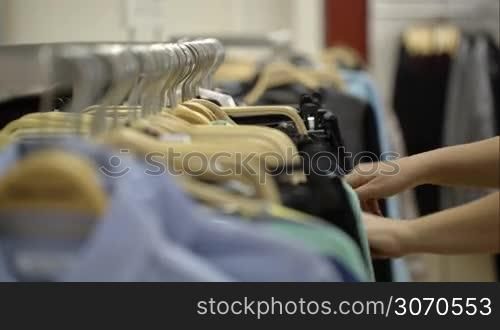 Close-up shot of a woman in the store looking over clothes hanging on the racks, she taking one thing to try