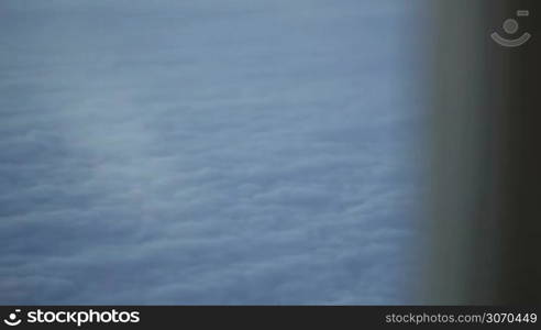 Close-up shot of a woman looking out illuminator in a plane, solid clouds beneath. At first focus on clouds, then on woman