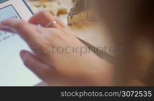 Close-up shot of a woman making cookies checking recipe on tablet computer. She cutting out a star shape from the dough