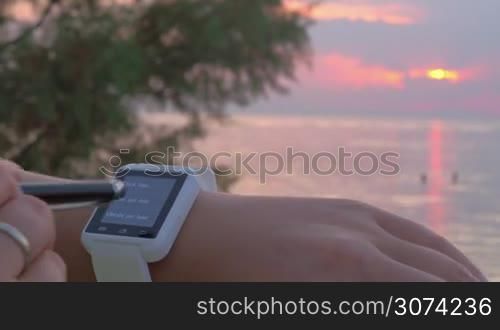 Close-up shot of a woman setting right date on the smart watch outdoor. Sunset and sea as background