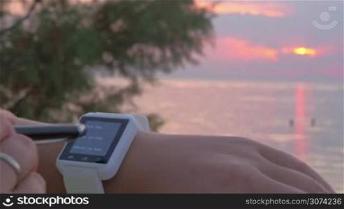 Close-up shot of a woman setting right date on the smart watch outdoor. Sunset and sea as background