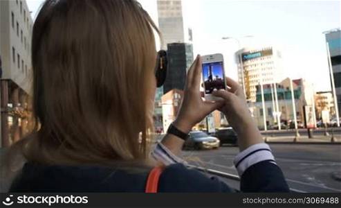 Close-up shot of a woman taking pictures of modern city buildings using her smartphone