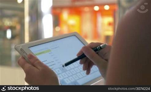 Close-up shot of a woman typing message or taking notes on tablet computer at the airport of shopping mall