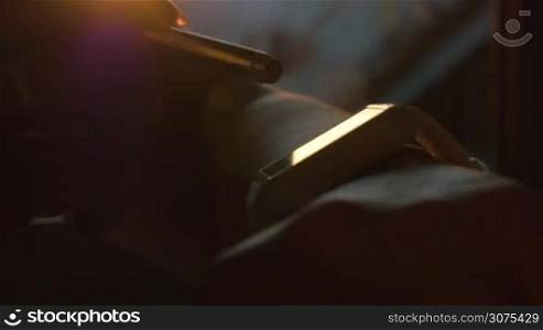 Close-up shot of a woman using smart watch with pen standing by the window at sunset