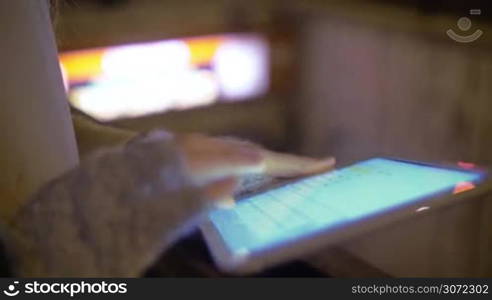 Close-up shot of a woman using tablet computer by the underground entrance in the street at night. LED-display panel with information above the entry. At first focus on pad, then on display