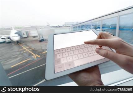 Close-up shot of a woman using touch pad with clear white screen at the airport. Boarding plane in background