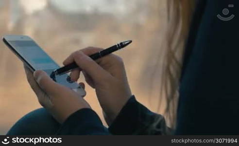 Close-up shot of a woman with pen typing sms or email on touchscreen smartphone while traveling by train. Communication makes journey more enjoyable