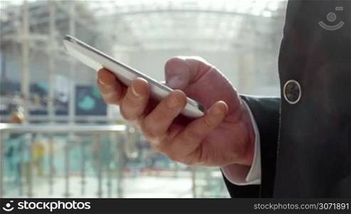 Close-up shot of a young businessman typing text message on smartphone in modern office building or shopping centre