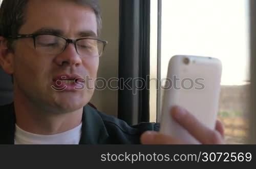Close-up shot of a young smiling businessman having a video call during train traveling
