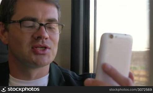 Close-up shot of a young smiling businessman having a video call during train traveling