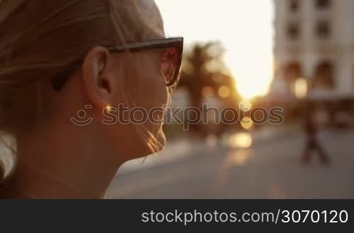 Close-up shot of a young smiling woman in sunglasses outdoor. She looking somewhere, then turning and smiling and looking away again
