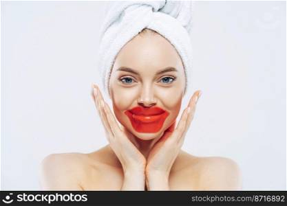 Close up shot of attractive young woman touches cheeks gently, applies collagen patches for dry lips, enjoys beauty routine at home after taking shower, uses korean cosmetics, poses naked indoor