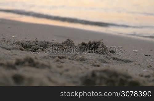 Close-up shot of beach sand and sea waves rolling on the shore at sunset
