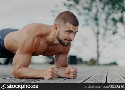 Close up shot of bearded motivated man stands in plank, trains muscles and wants to have strong body. Sportsman doing exercises outdoor. Athletic guy does push ups. Sport and lifestyle concept