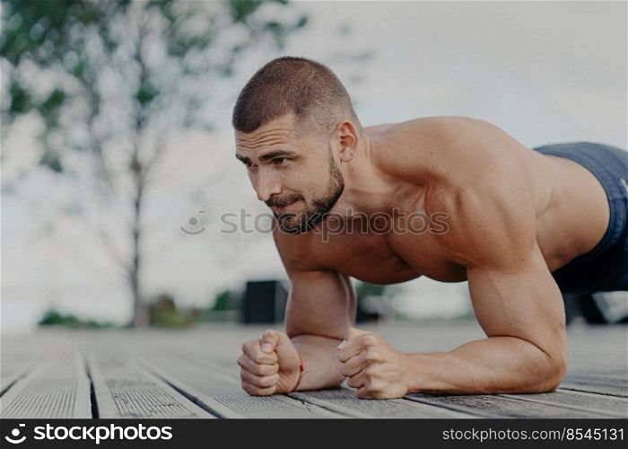 Close up shot of bearded motivated man stands in plank, trains muscles and wants to have strong body. Sportsman doing exercises outdoor. Athletic guy does push ups. Sport and lifestyle concept