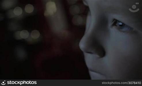 Close-up shot of boy face in the darkness with TV screen reflection in the eyes
